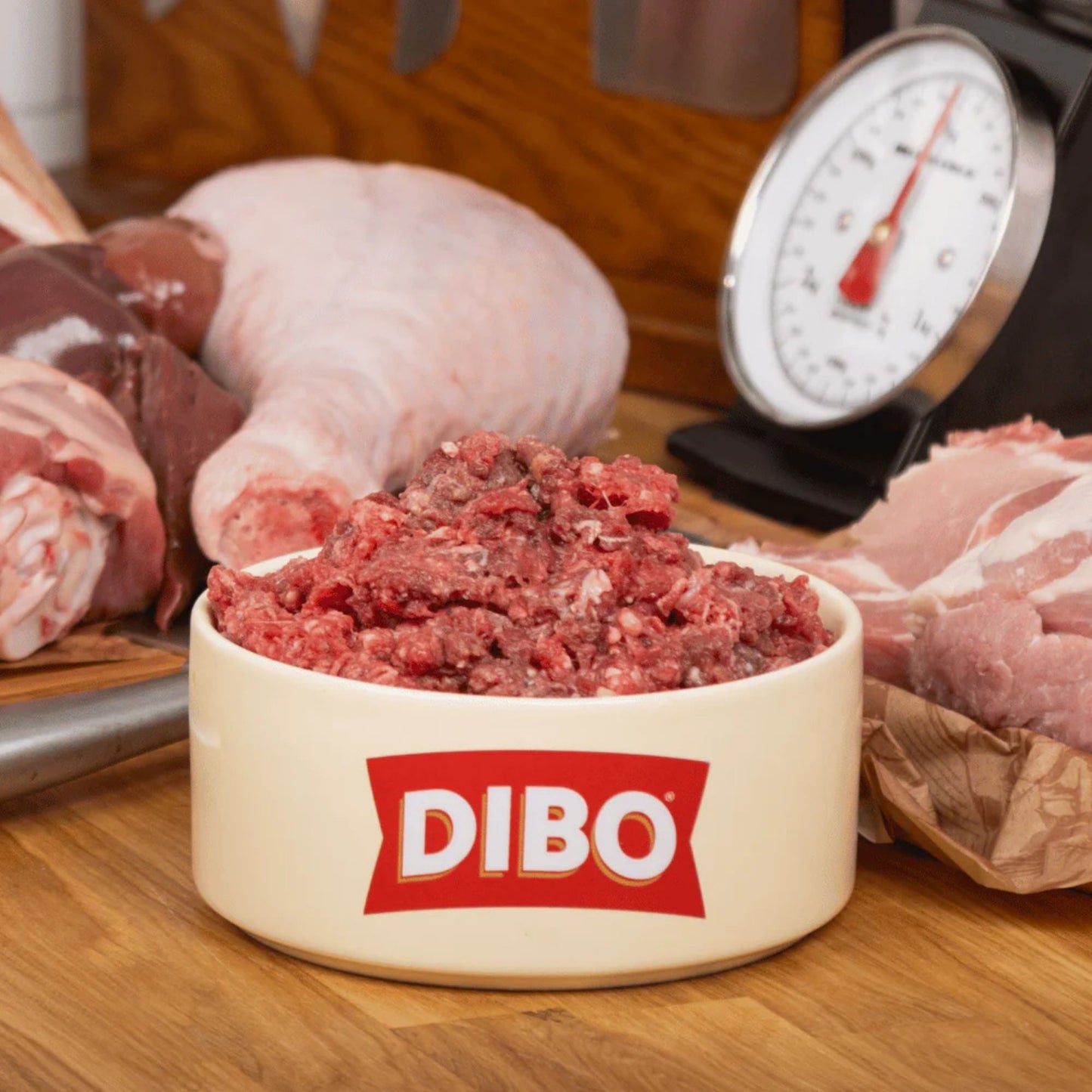 Bowl of ground meat with DIBO logo on a wooden surface with raw meat in the background.