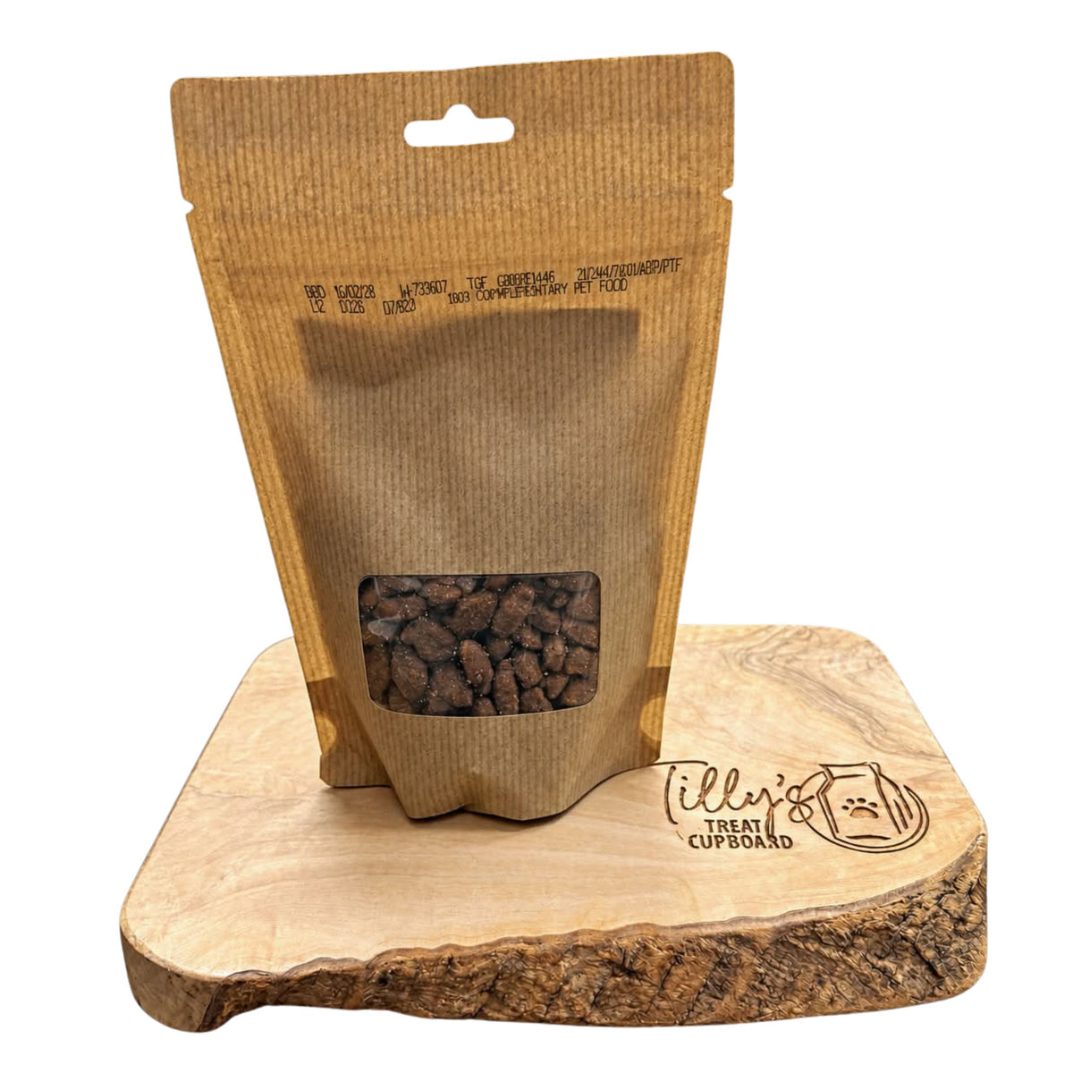 A brown kraft paper stand-up pouch with a clear window showing kibble, displayed on a wooden slice board with the brand name 'Till's Cupboard' printed on it, against a white background.