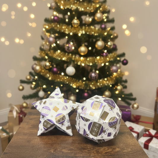 Decorative paper fish with Christmas ornaments on a wooden surface, with tennis balls and boxes in the background.