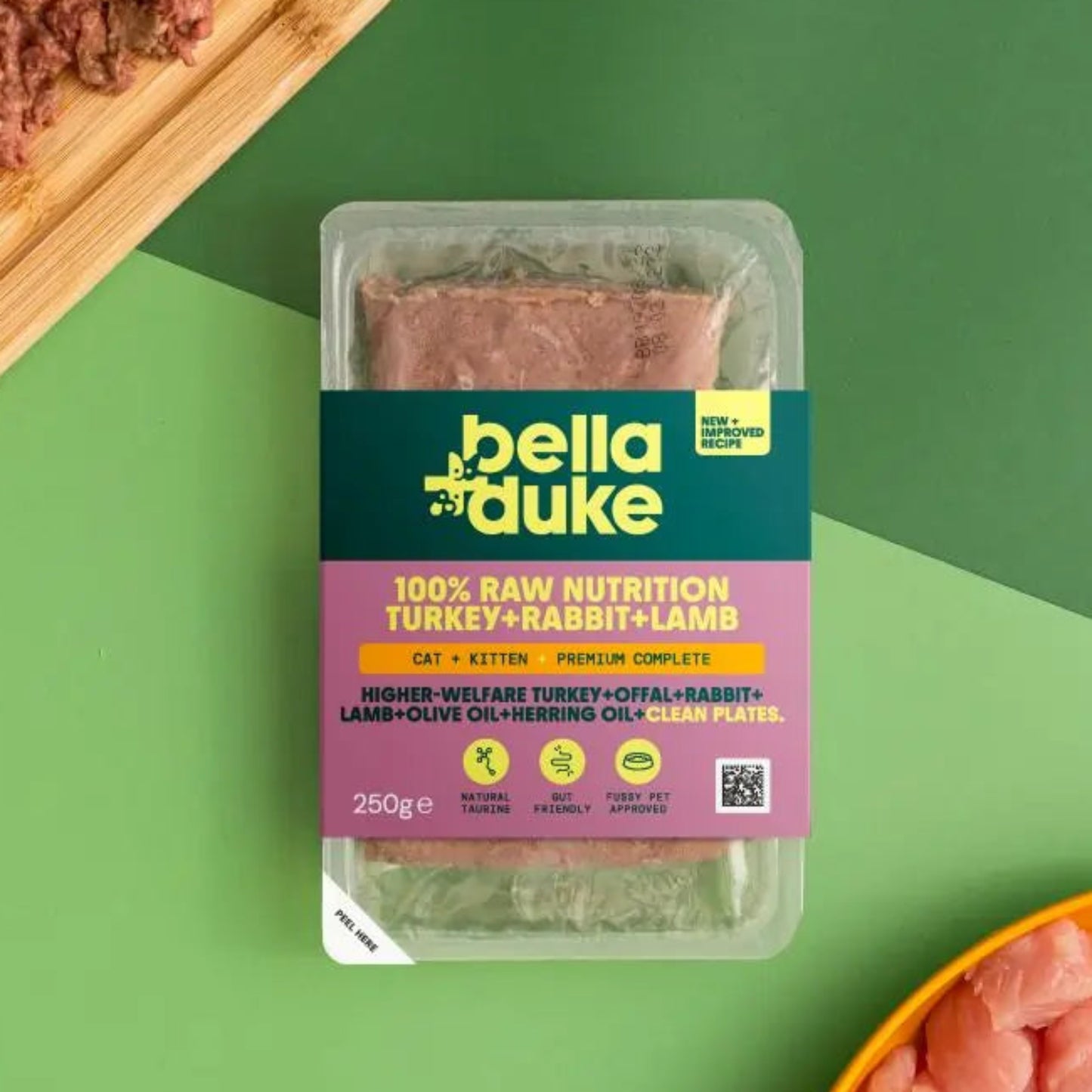 Bella Duke pet food packaging on a green background with raw pet food on a cutting board and in a bowl.