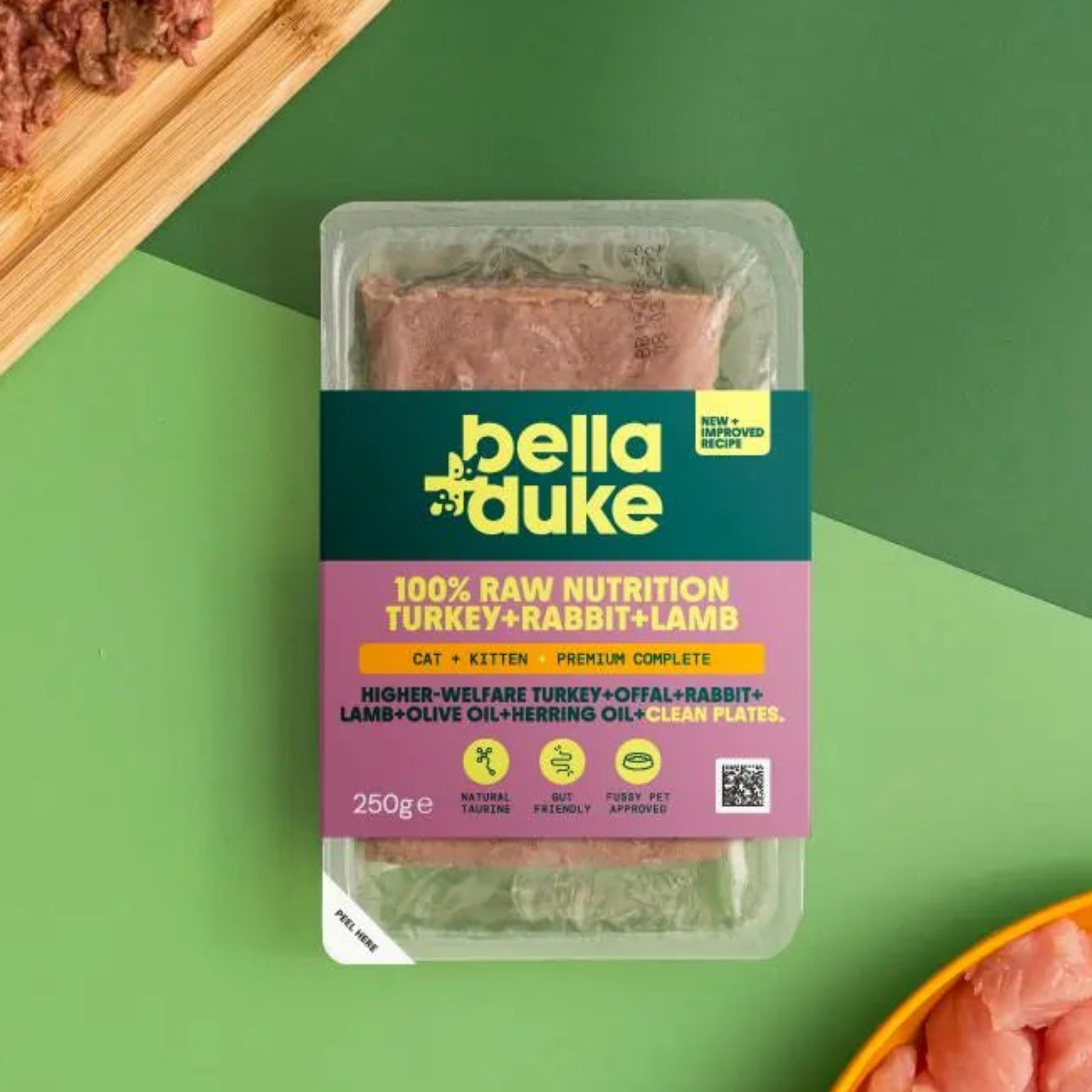 Bella Duke pet food packaging on a green background with raw pet food on a cutting board and in a bowl.