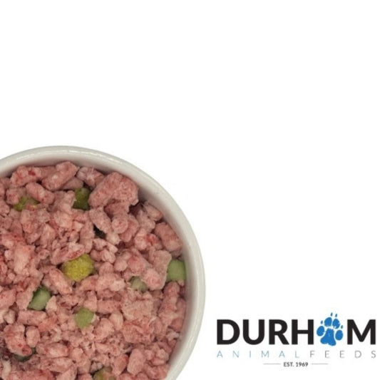 A top-down view of a white bowl filled with raw, pinkish meat-based pet food mixed with small green and yellow pieces, set against a white background with the Durham Animal Feeds logo in the bottom right corner.