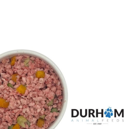 A top-down view of a white bowl filled with pinkish raw pet food containing small yellow and green vegetable pieces, with the Durham Animal Feeds logo in the bottom right corner on a white background.