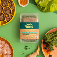 Bella+Duke pet food packaging surrounded by raw ingredients on a green background