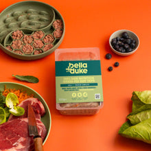 Bella Duke pet food packaging on an orange background with raw meat and vegetables.