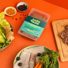 Bella Duke pet food packaging on an orange background with ingredients around it.