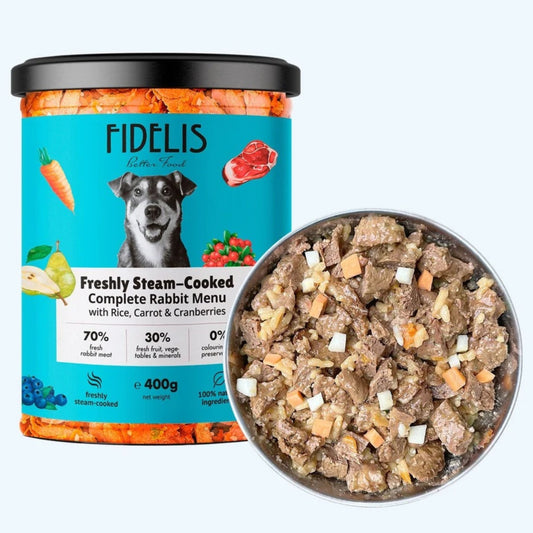 A jar of FIDÉLIS premium rabbit food with a black lid and turquoise label, shown next to a metal bowl filled with the cooked rabbit food. The label reads 'Freshly Steam-Cooked Complete Rabbit Menu with Rice, Carrot & Cranberries' and shows a dog illustration.