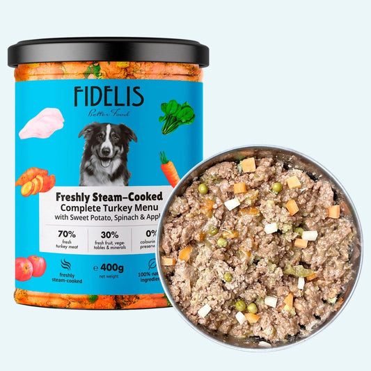 A tub of FIDELIS Freshly Steam-Cooked Complete Turkey Menu dog food next to a metal bowl filled with the cooked wet food, on a pale blue background.