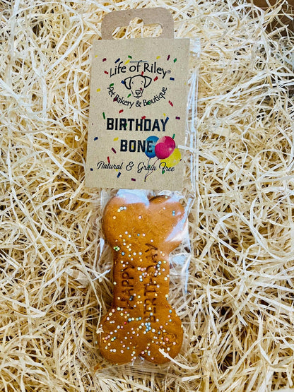 Dog bone-shaped treat with 'Happy Birthday' text on a straw background, branded 'Life of Riley'.