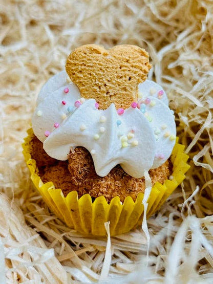 Dog treat shaped like a heart with white icing and sprinkles on a bed of straw.