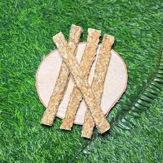 Four textured redfish skin stick treats arranged in an X and vertical line on a round light wood slice, placed on bright green artificial grass with a green leaf prop.