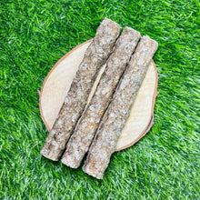 Three seabass chew sticks with bark texture, arranged on a round wooden slice over a bright green grass-like background.