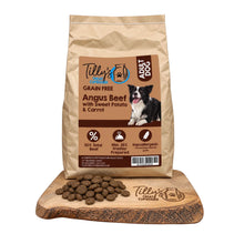 A bag of Tilly's Treat Cupboard Grain Free Adult Dog food in Angus Beef with Sweet Potato & Carrot, displayed on a wooden cutting board with kibble pieces in front, against a white background.