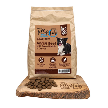 A bag of Tilly's Treat Cupboard Grain Free Adult Dog food in Angus Beef with Sweet Potato & Carrot, displayed on a wooden cutting board with kibble pieces in front, against a white background.