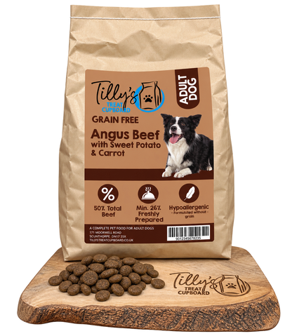 A bag of Tilly's Treats Cupcake Adult Dog grain-free dog food stands on a wooden cutting board with kibble pieces scattered in front. The bag is kraft brown with a large tan label featuring a black-and-white dog photo and product text.