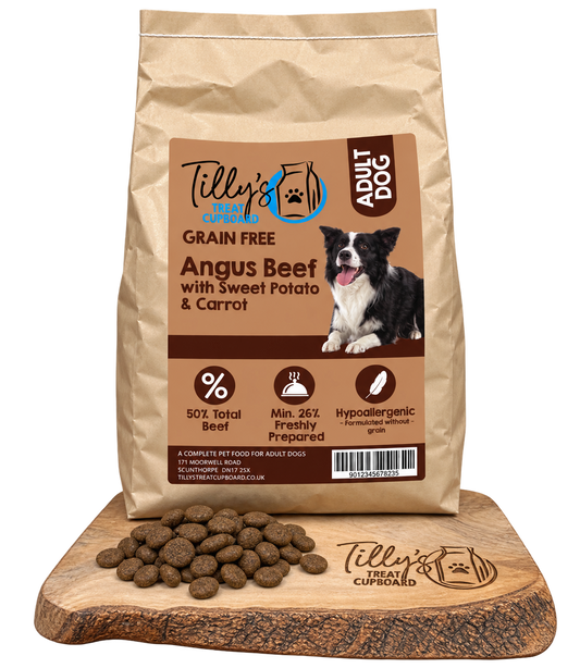 A bag of Tilly's Treats Cupcake Adult Dog grain-free dog food stands on a wooden cutting board with kibble pieces scattered in front. The bag is kraft brown with a large tan label featuring a black-and-white dog photo and product text.