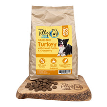 A bag of Tilly's Treat Cupboard Adult Dog grain-free turkey with sweet potato & cranberry kibble stands on a wooden board with loose kibble pieces in front, against a plain white background.