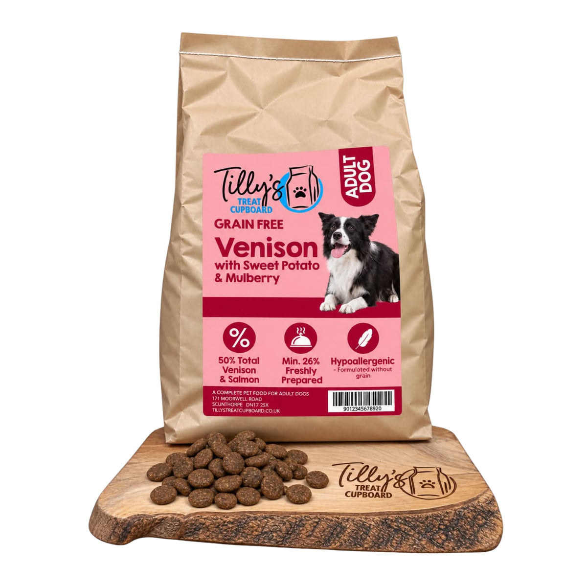 A bag of Tilly's Treat Cupboard Adult Dog grain-free venison kibble stands upright on a wooden board with loose kibble pieces in front. The package is kraft paper with a large pink front label showing the brand, product type, and a dog photo.