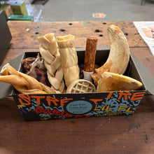 Box of pet treats with various items on a wooden surface