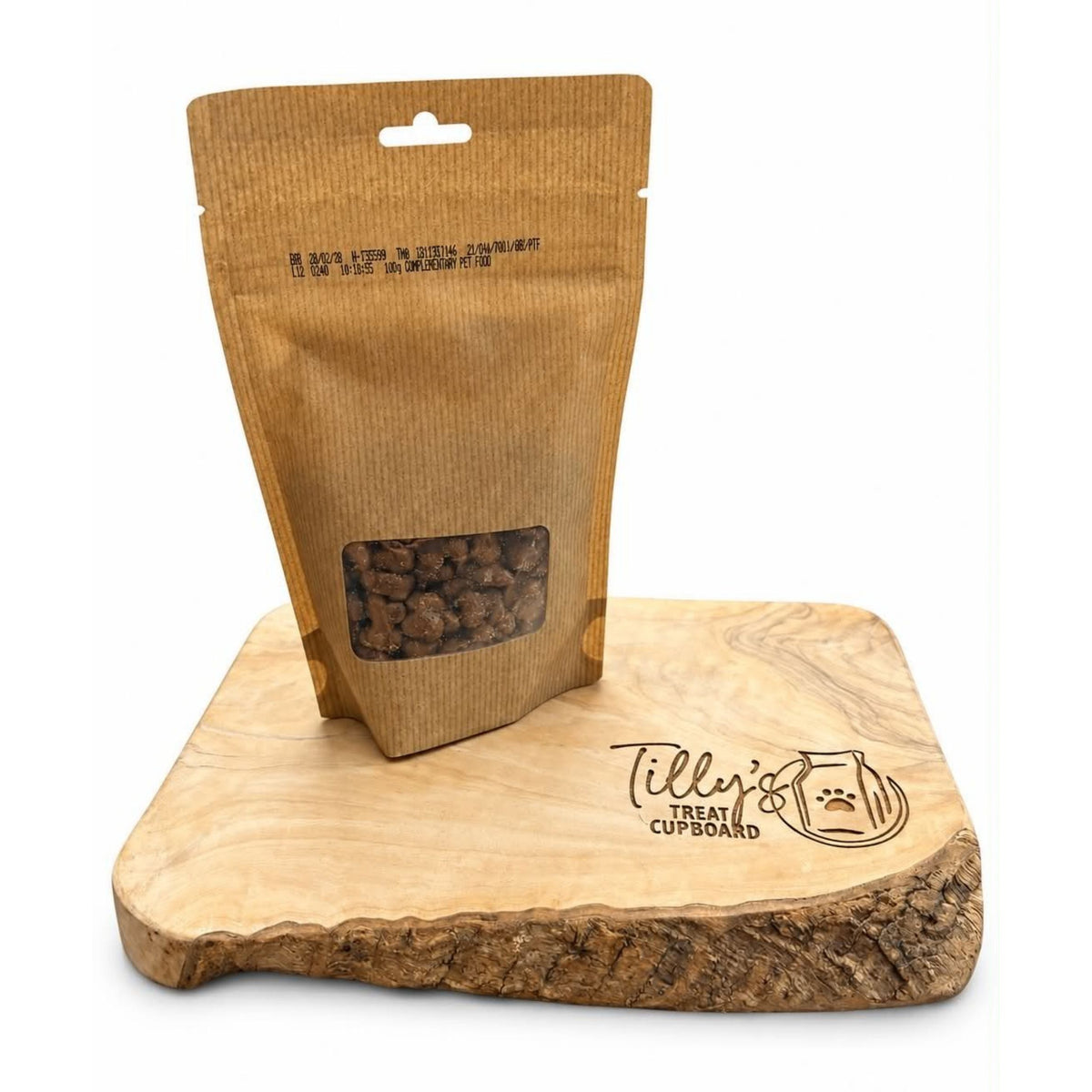 A brown kraft paper stand-up pouch with a clear window showing dog treats, displayed on a wooden treat cupboard with the brand name 'Tilly's' engraved on the front.