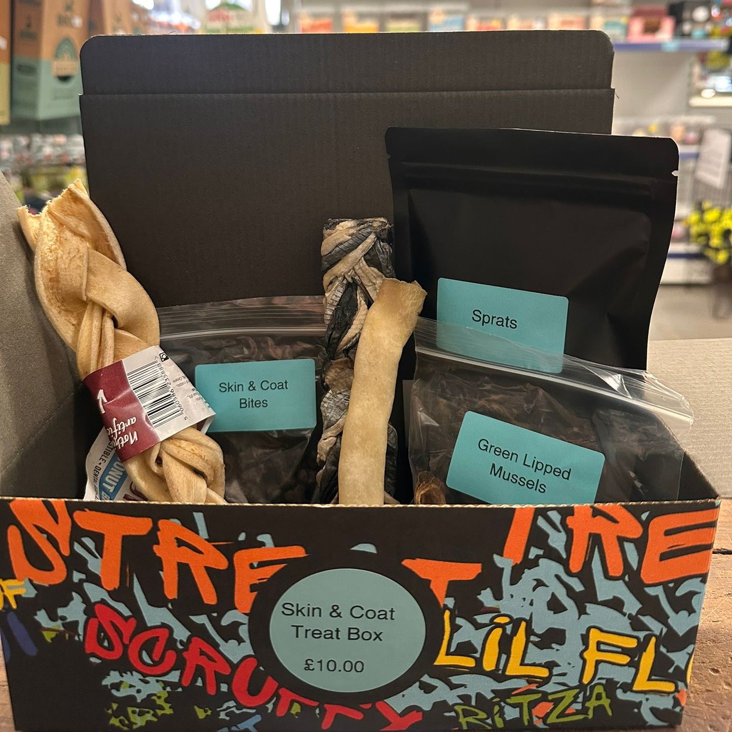 Dog treat box with various treats and packaging labeled 'Sprats', 'Skin & Coat Bites', and 'Green Lipped Mussels' in a store setting.