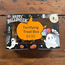 A Halloween-themed treat box on a rustic wooden table. The black box features 'Happy Halloween' text, ghost illustrations, jack-o'-lanterns, and a large orange label in the center that reads 'Terrifying Treat Box £4.