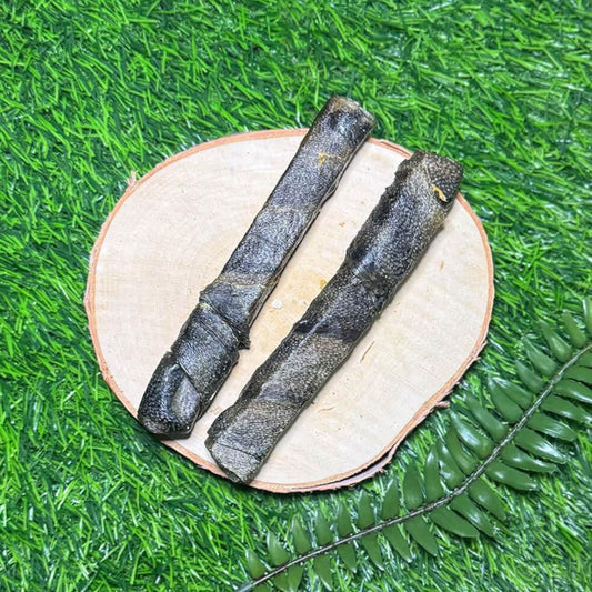 Two dark wolf fish sticks placed on a round light wood slice, set on bright green artificial grass with a fern leaf in the foreground.