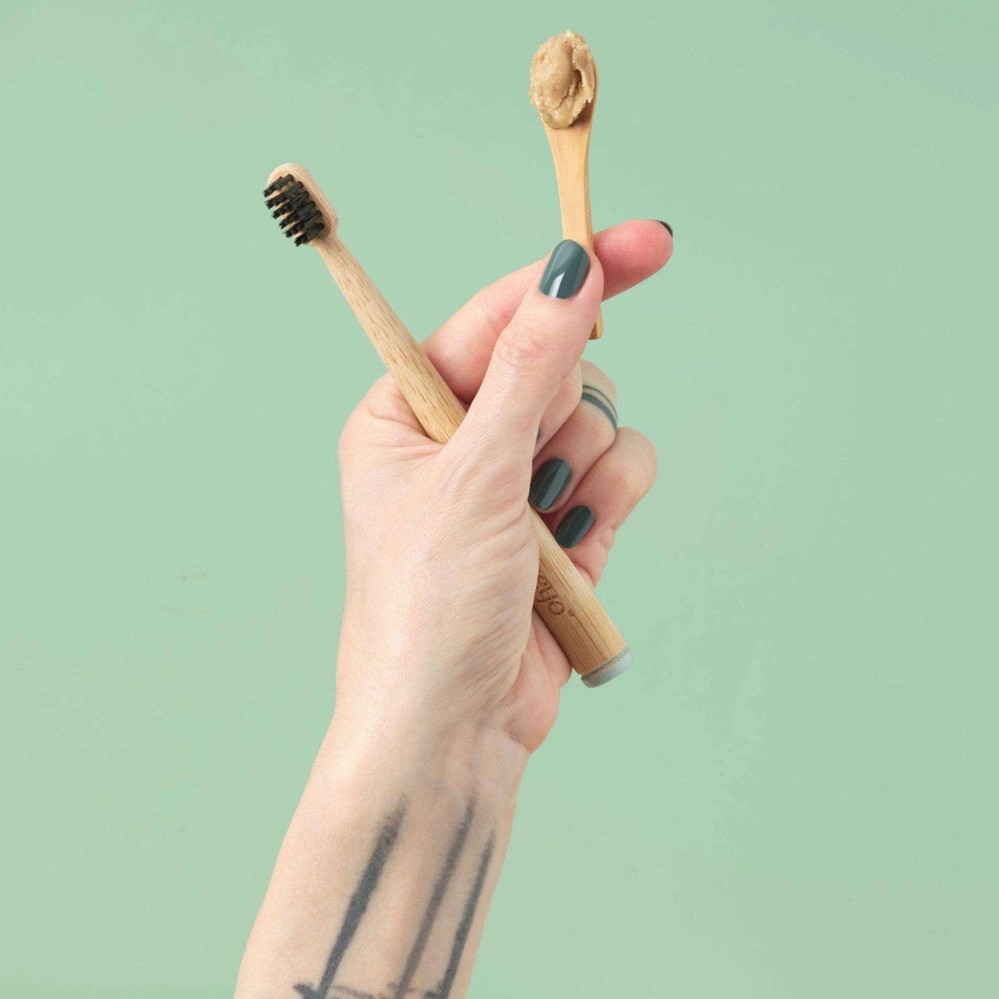 Hand holding two wooden toothbrushes with a green background