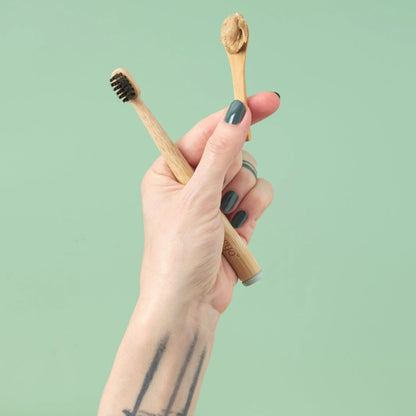 Hand holding two wooden toothbrushes with a green background